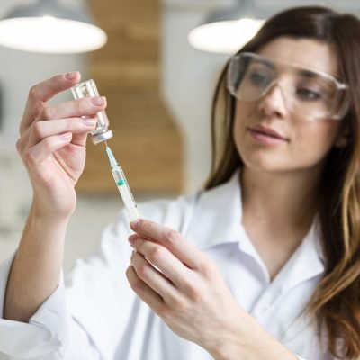 female-scientist-with-safety-glasses-holding-syringe-with-vaccine-lab